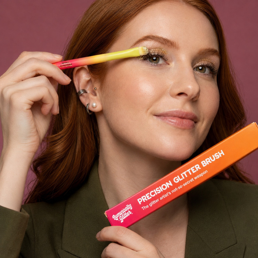 Woman applying makeup with a precision glitter brush against a purple background