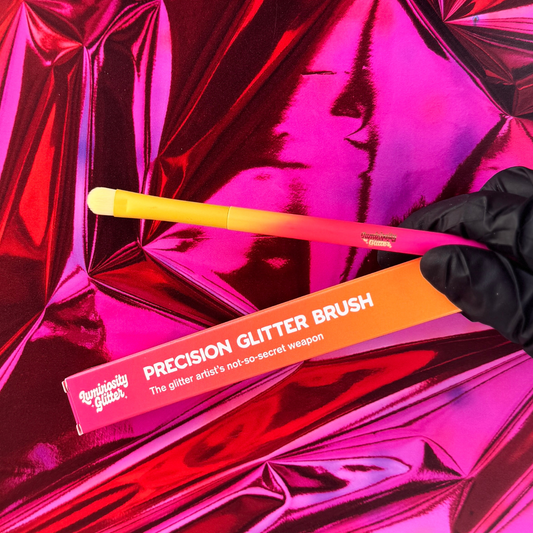 Precision glitter brush with orange handle and packaging on pink reflective background