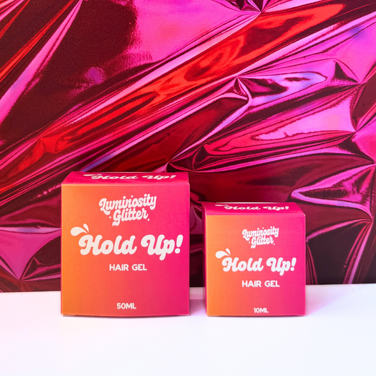Two boxes of Luminosity Glitter Hold Up Hair Gel against a pink textured background