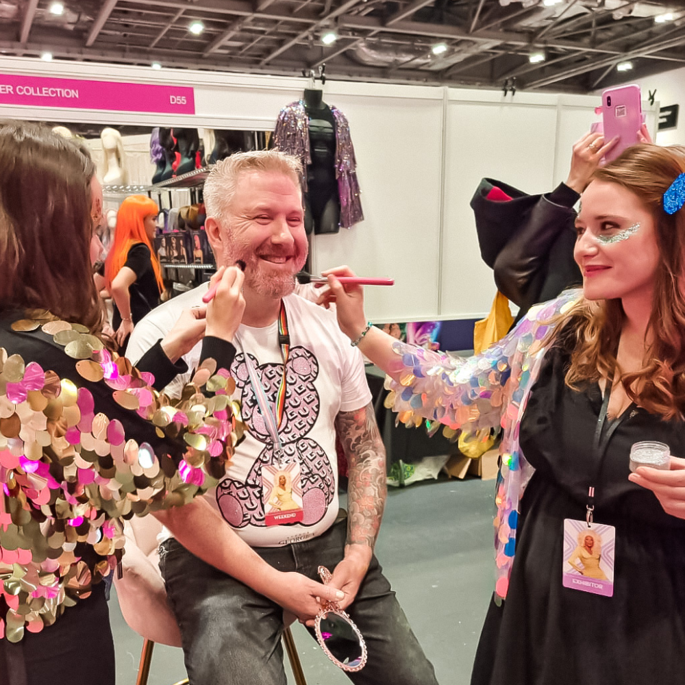 Glitter artists at Drag Con UK glittering a customers beard with pink glitter