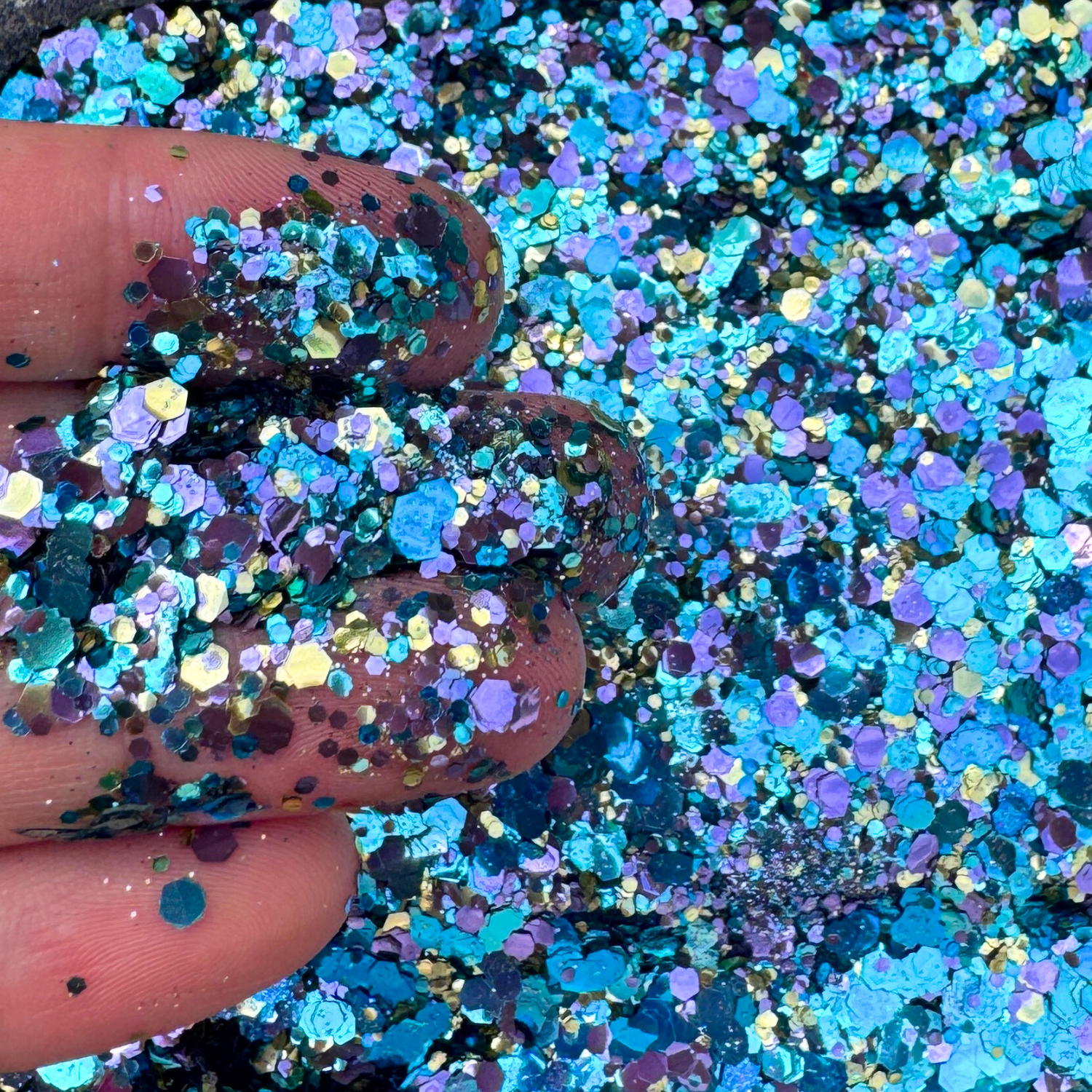 Close-up of blue and purple glitter with a finger holding some glitter.