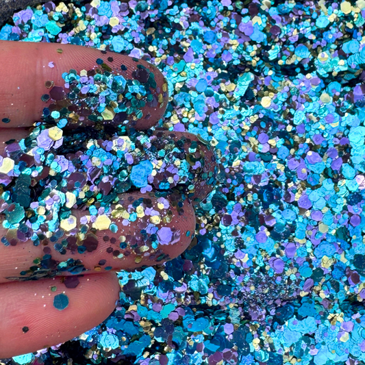 Close-up of blue and purple glitter with a finger holding some glitter.