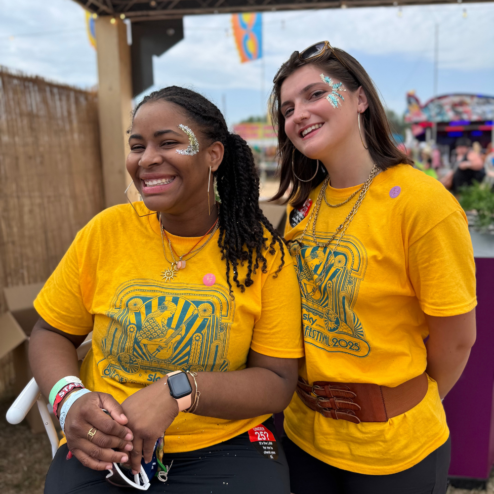 Two women wearing yellow t-shirts with a tiger design at an outdoor event.