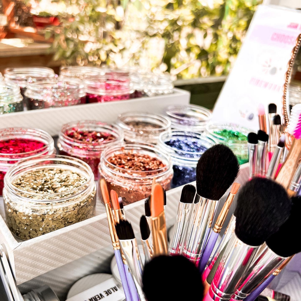 Makeup brushes and containers of glitter on a table with a blurred outdoor background