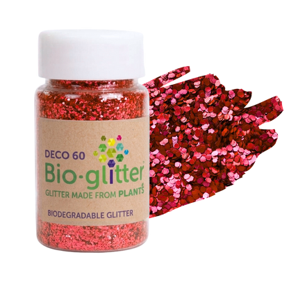 A clear plastic jar of chunky craft Bio-glitter with a white cap and a kraft paper label, shown next to a fan of red and pink plant-based glitter on a white background.