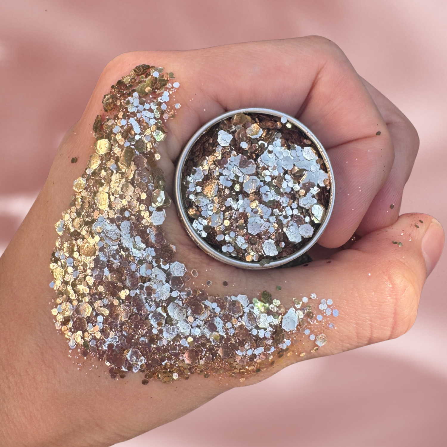 Hand holding glitter with a small container of glitter on a pink background