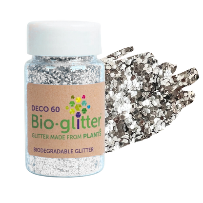 A clear plastic jar of chunky silver craft Bio-glitter with a white cap and a brown paper label, shown next to a pile of reflective silver glitter pieces on a white background.